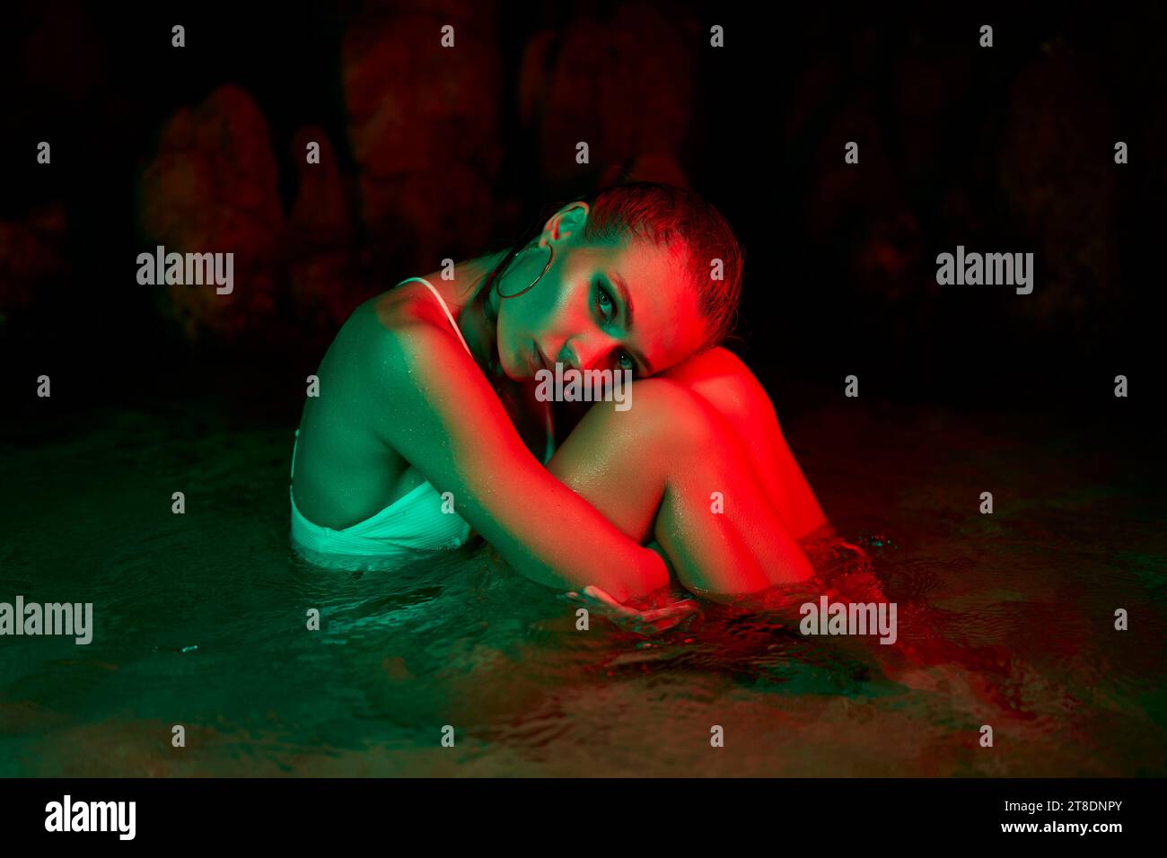 Frau tauchte nachts in die Lagune ein, leuchtende grüne und rote Lichter. Introspektion und emotionales Tiefenthema in ruhiger Umgebung. Konzeptuelles Kunstwerk Stockfoto