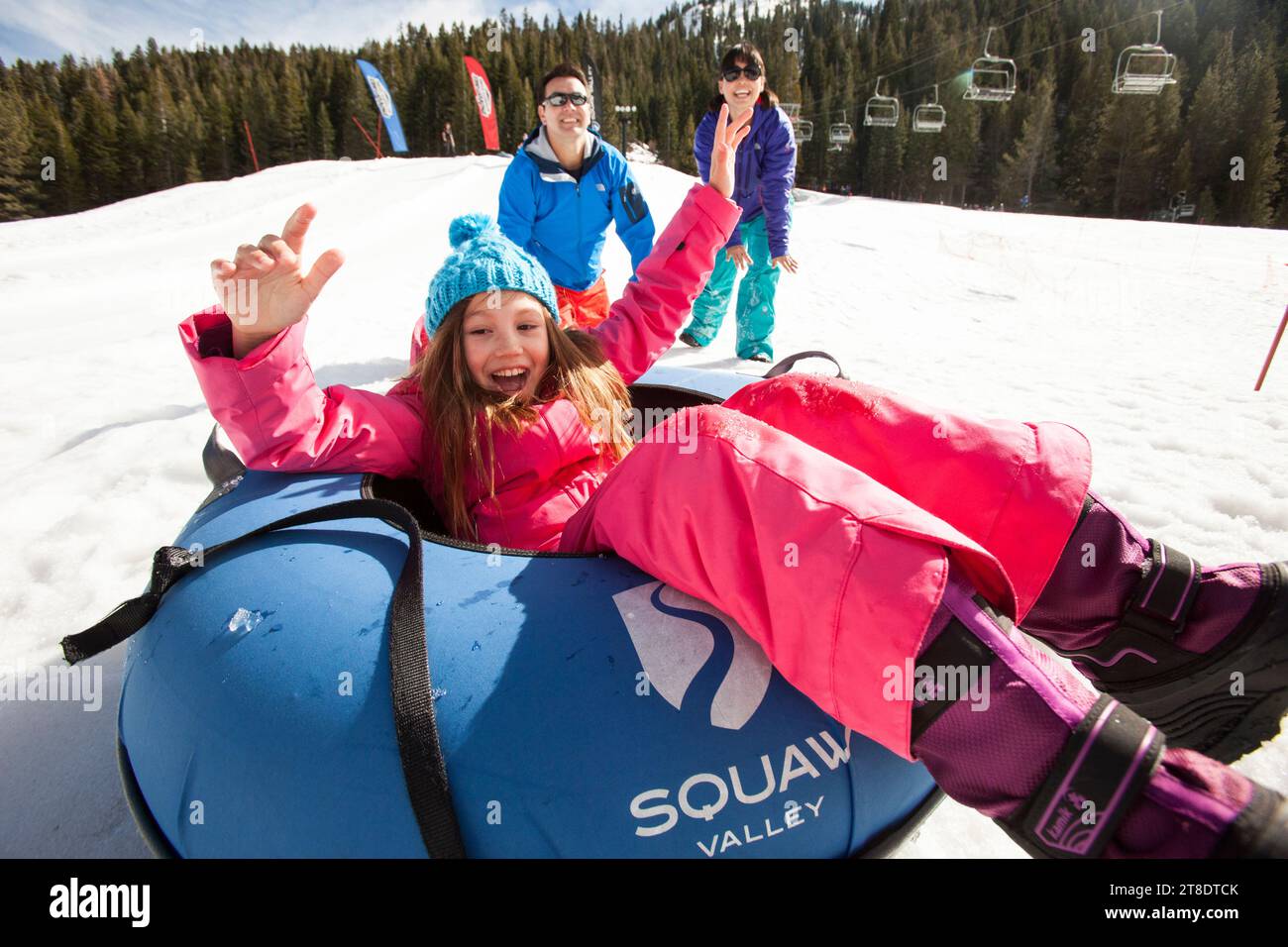 Eltern schieben ein junges Mädchen in einem Skigebiet auf eine Tube. Stockfoto