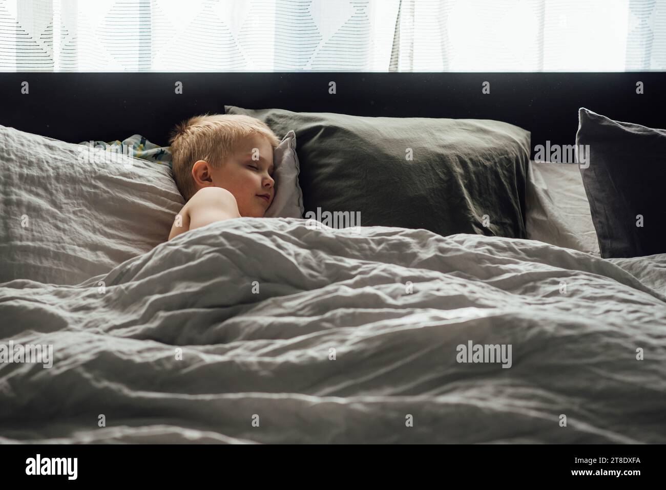 Großer Blick auf einen kleinen Jungen, der friedlich ein Nickerchen auf einem großen Bett mit n macht Stockfoto