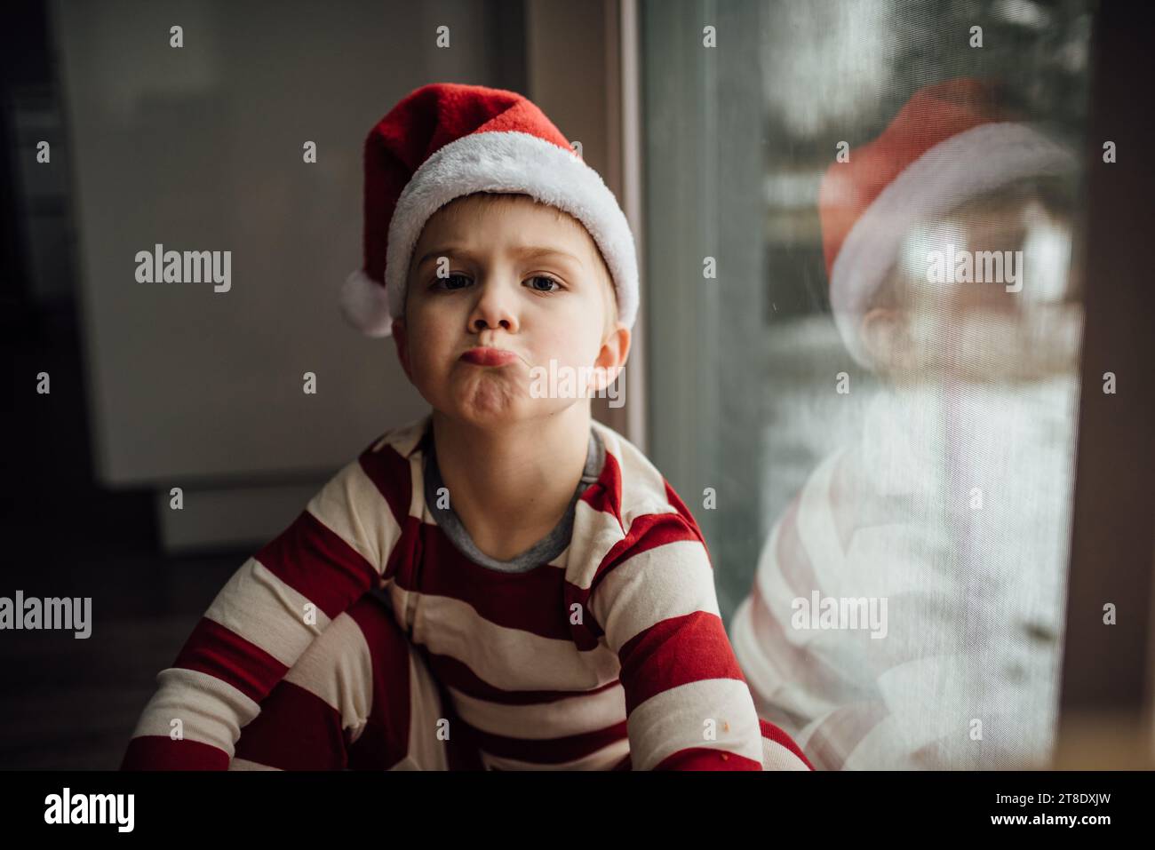 Der kleine Junge schaut in die Kamera und schmeckt, während er weihnachts-paj trägt Stockfoto