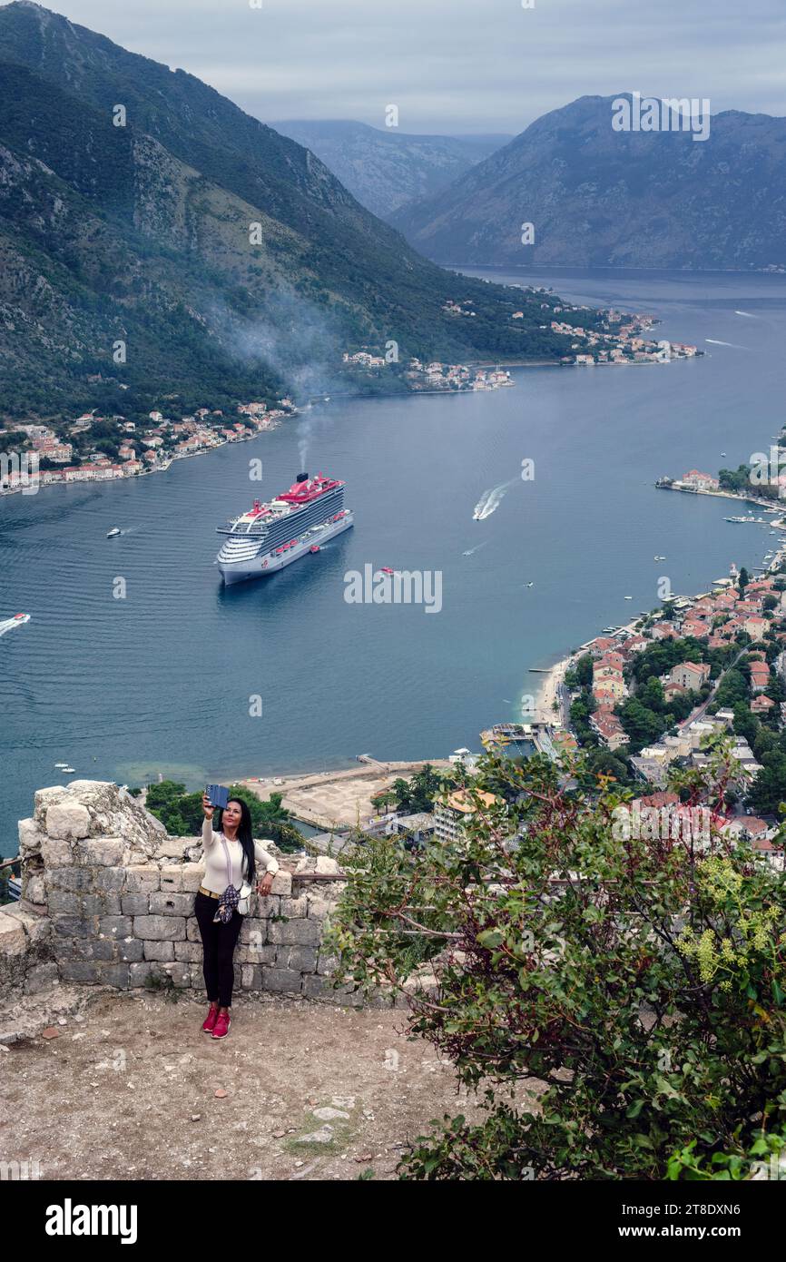 Ein Tourist macht ein Selfie in der Festung Kotor mit der Kulisse eines Kreuzfahrtschiffs in der Bucht von Kotor, Montenegro, 2023 Stockfoto