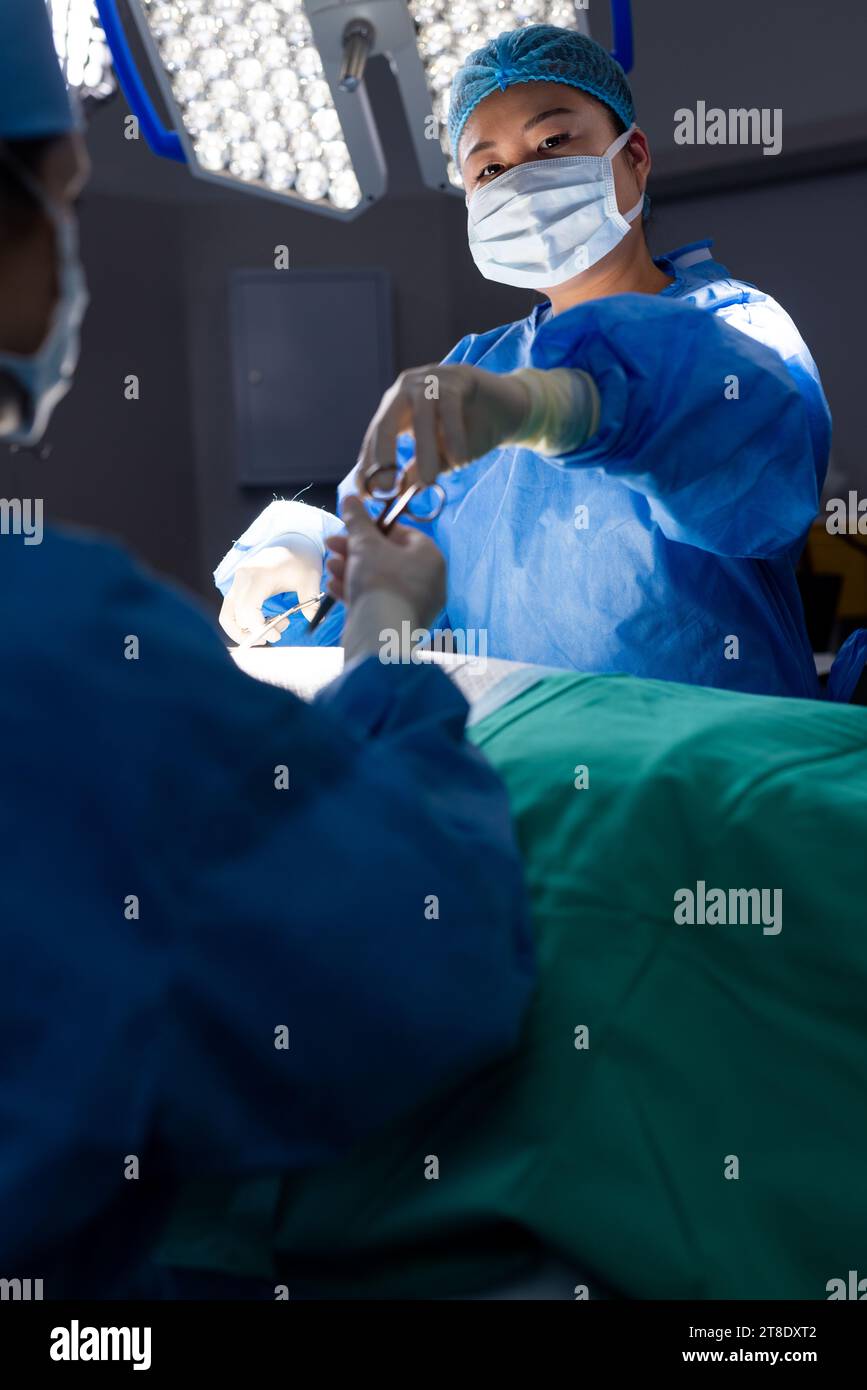 Diverse Ärztin mit Gesichtsmaske in der Gruppe von Ärzten im Krankenhausoperationssaal Stockfoto