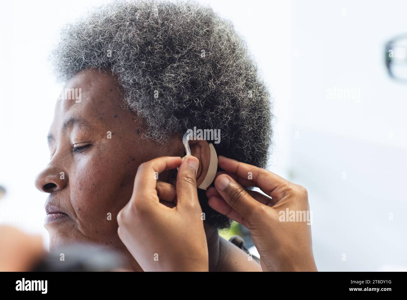 Hände einer afroamerikanischen Ärztin, die Hörgeräte bei Seniorinnen im Krankenhauszimmer anwendet Stockfoto