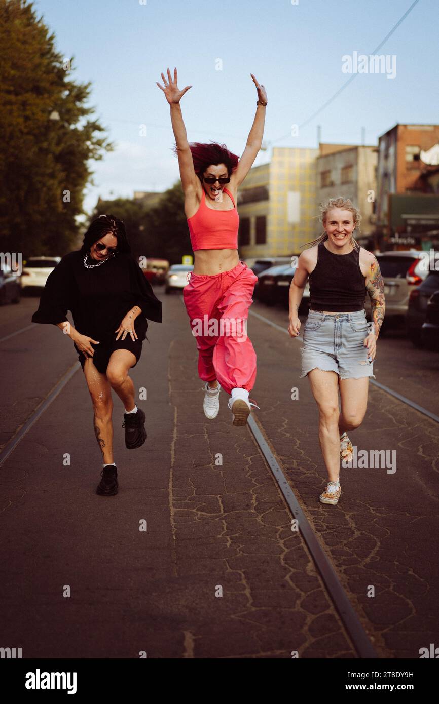 Drei glückliche Freundinnen rennen die Straße runter und springen hoch. Stockfoto