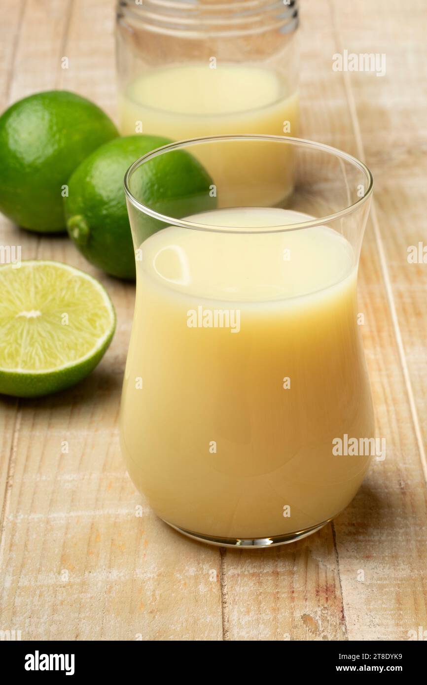 Trinkglas mit Limettensaft und frischen grünen Limetten auf dem Tisch Stockfoto