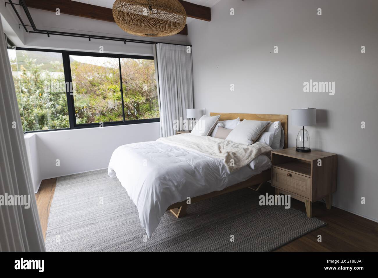 Großes leeres Schlafzimmer mit weißem Bett, Holzschrank und großen Fenstern Stockfoto