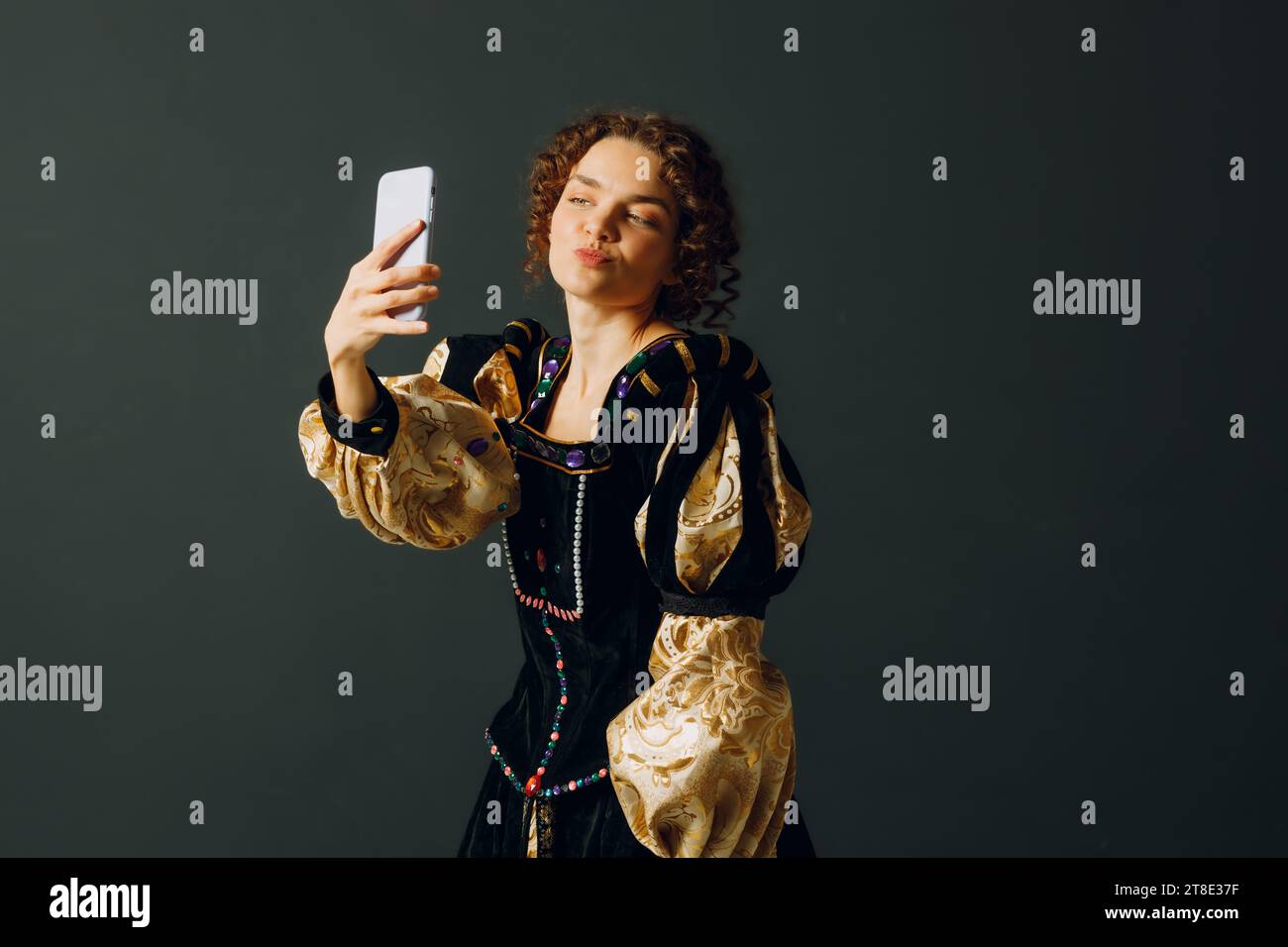 Porträt einer jungen aristokratischen Frau, die ein Handy in mittelalterlichem Kleid hält und Selfie macht Stockfoto