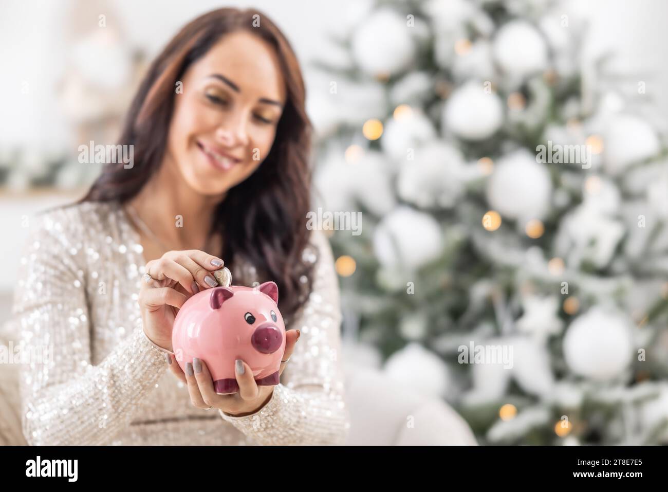 Frau spart Geld für Weihnachten, während sie eine 2-Euro-Münze in eine Sparbank steckt. Stockfoto