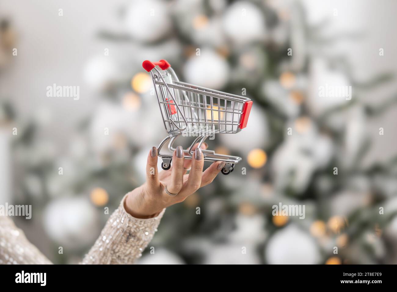 Weibliche Hand, die einen kleinen Einkaufswagen als Symbol der Weihnachtszeit hält. Stockfoto