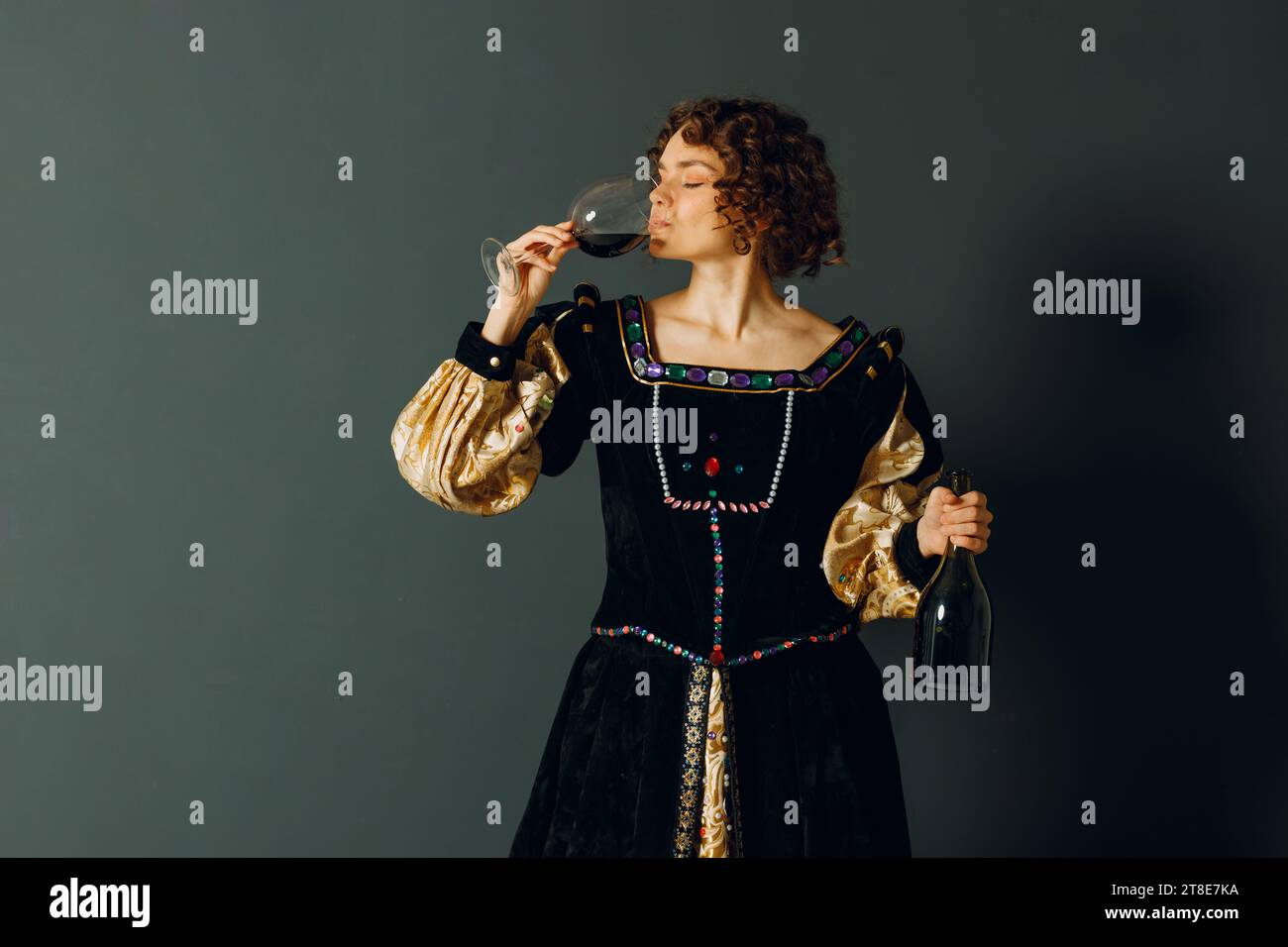 Junge Erwachsene Frau in einem mittelalterlichen Kleid, die ein Glas Wein hält Stockfoto