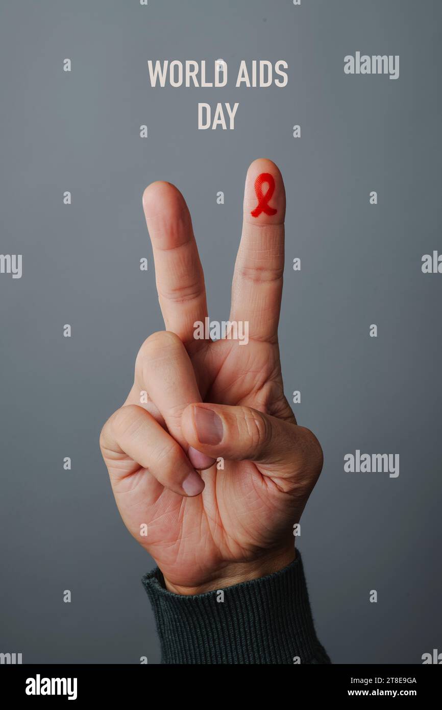 Nahaufnahme der Hand eines Mannes, der das V-Zeichen mit einem roten Wahrnehmungsband macht, für den Kampf gegen AIDS, im Zeigefinger gemalt, auf grauem Hintergrund Stockfoto