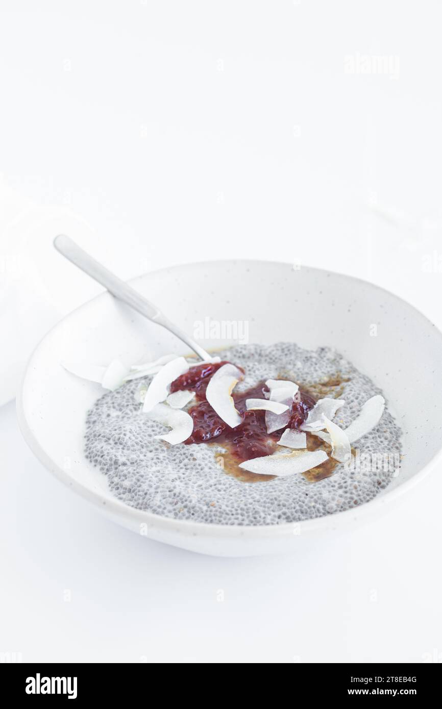Chia Pudding mit Marmelade und Kokoschips auf einer weißen Platte, Nahaufnahme. Veganes Frühstückskonzept. Stockfoto