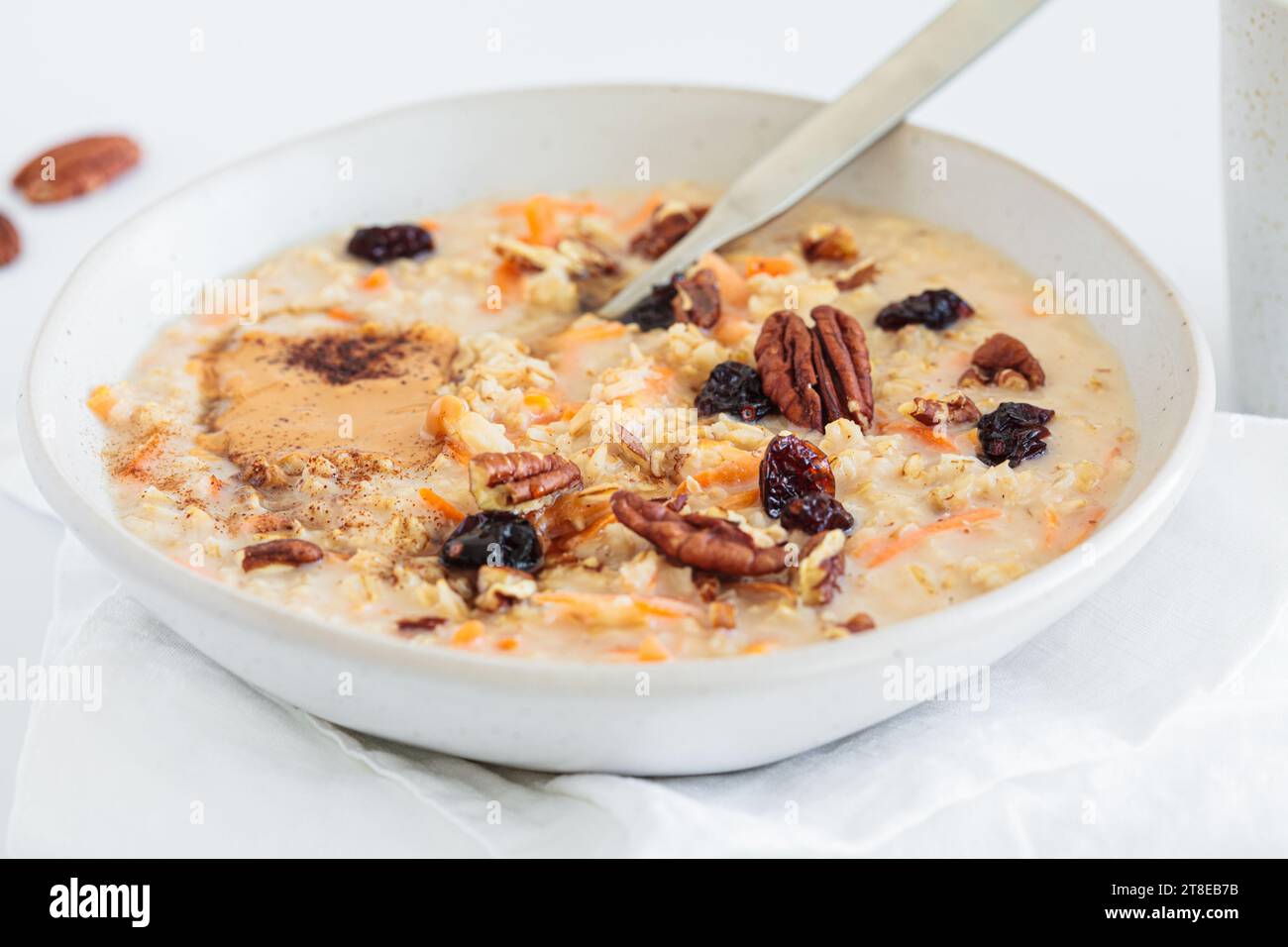 Karottenkuchen Haferflocken mit getrockneten Preiselbeeren, Pekannüssen und Erdnussbutter auf einer weißen Platte, weißer Hintergrund. Nahrhaftes gesundes Winterfrühstückskonzept. Stockfoto
