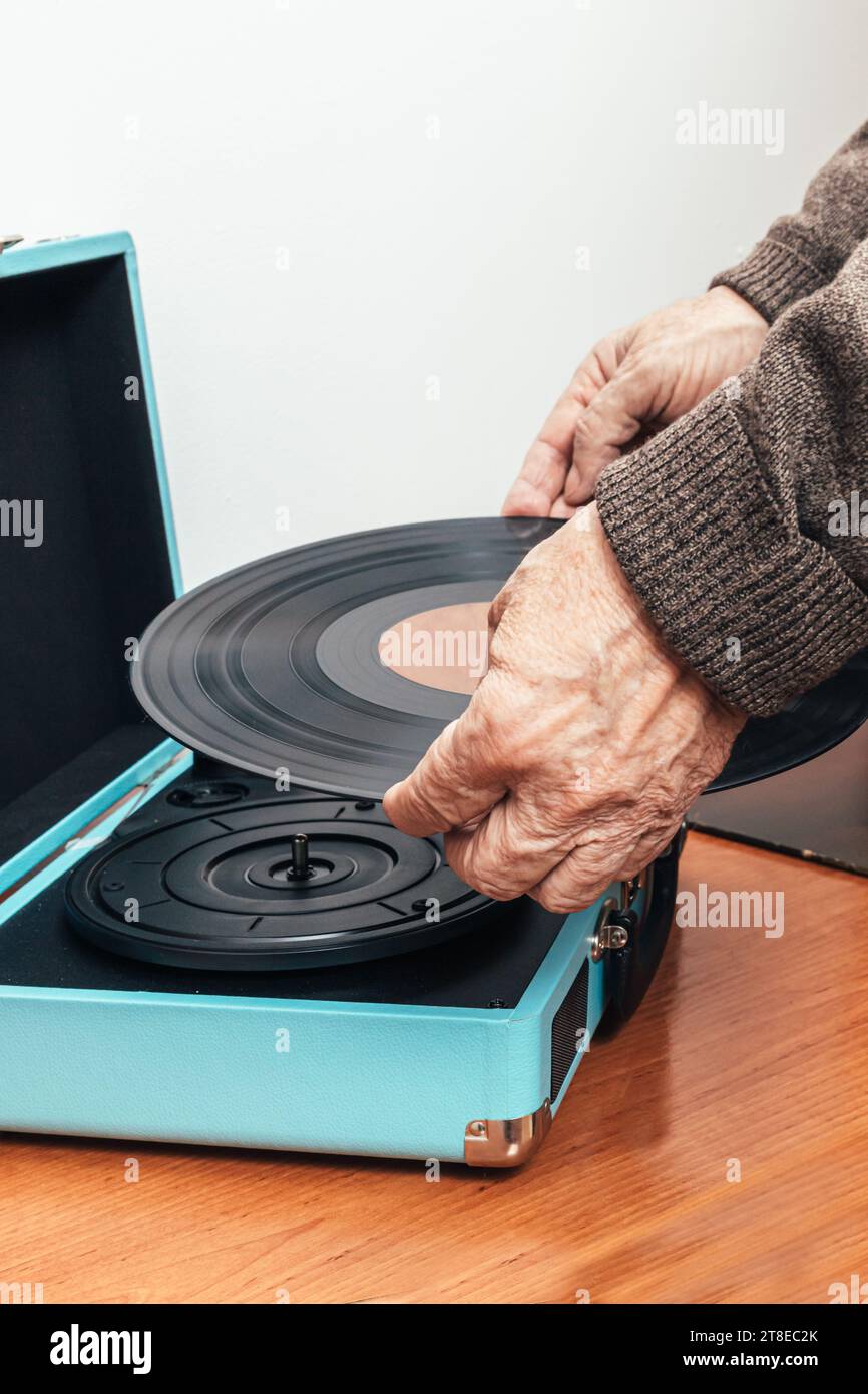 Vertikales Nahaufnahme-Foto, männlicher älterer Erwachsener, Kaukasier, Rücken gedreht, in braunem Wollpullover gekleidet. Platzieren einer Musikvinyl auf einem Plattenspieler. Stockfoto