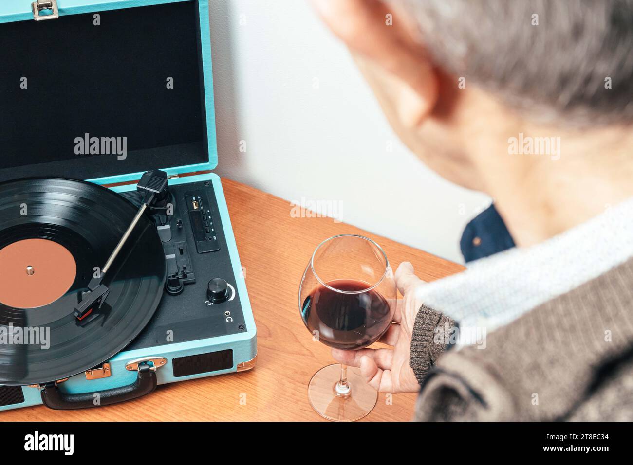 Horizontales Foto eines männlichen Mannes mit einem Glas Wein in der Hand, während er Musik von einem blauen Plattenspieler genießt. Konzepthobbys, Kunst. Stockfoto