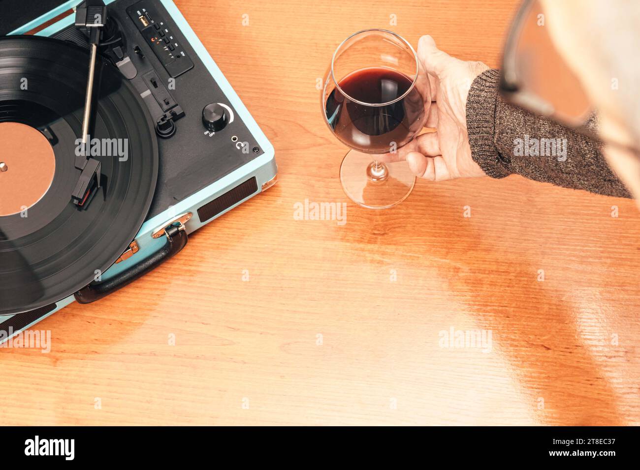 Horizontales Foto eines männlichen Mannes mit einem Glas Wein in der Hand, während er Musik von einem blauen Plattenspieler genießt. Kopierbereich. Stockfoto
