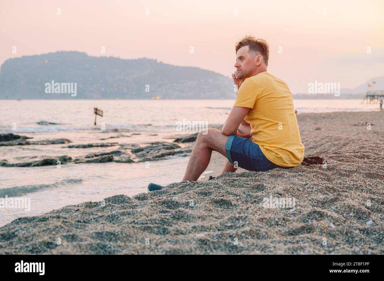 Der Mann sitzt am Strand und blickt auf das Meer in Alanya City, Türkei. Reise- oder Urlaubskonzept Stockfoto