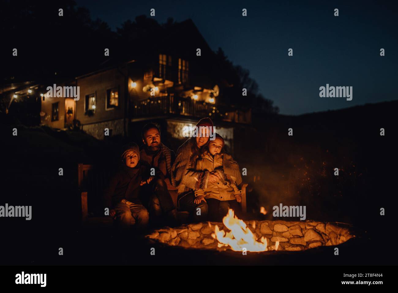Die Familie wärmt sich an einer Feuerstelle im Freien auf, sitzt in der abendlichen Wärme des Feuers und verbringt gute Familienzeit miteinander. Stockfoto