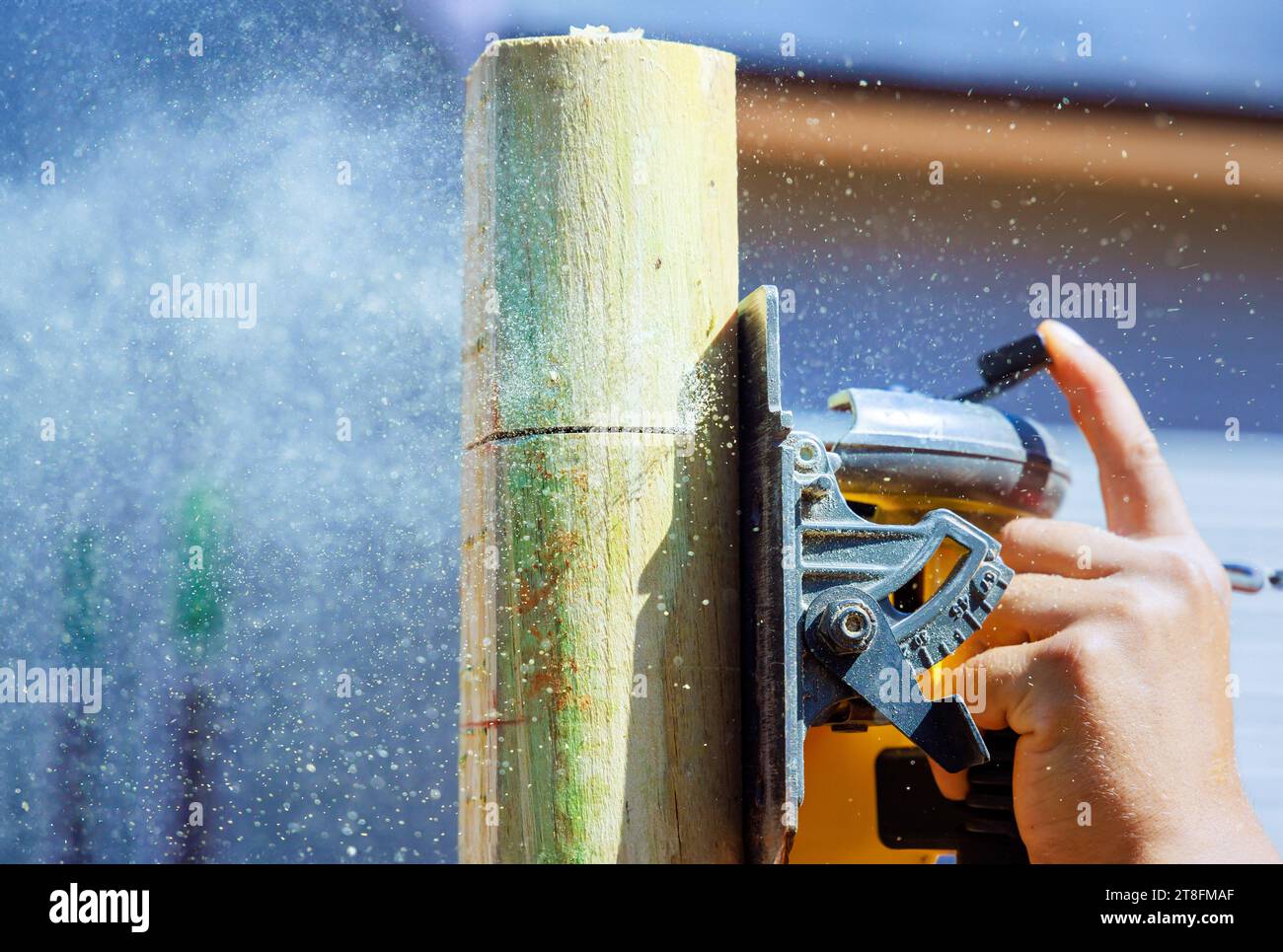 Eine elektrische Säge wird vom Arbeiter verwendet, um Holzpfosten für Zäune zu schneiden Stockfoto