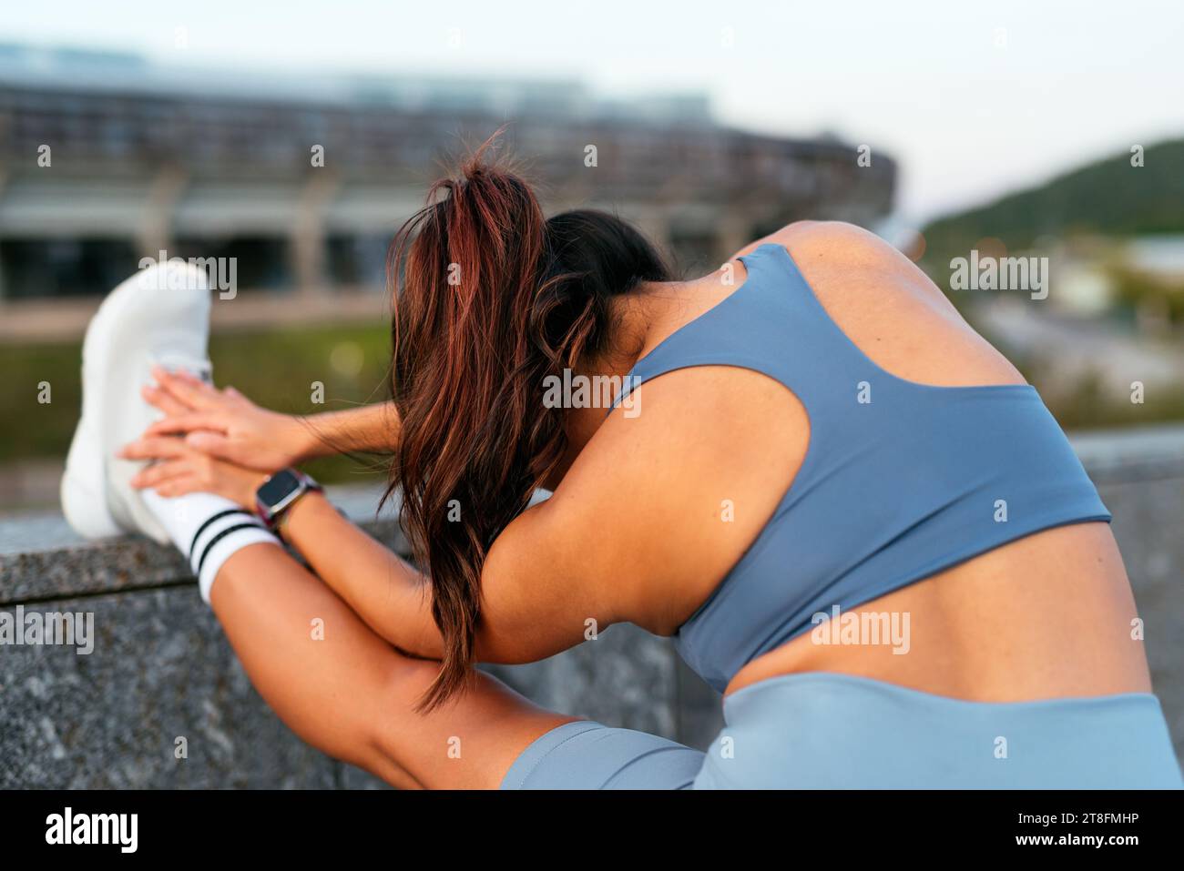 Lateinamerikanische Frau führt eine Oberschenkelmuskulatur-Dehnung vor einer Outdoor-Übung durch, die beispielhaft für einen gesunden Lebensstil ist. Stockfoto