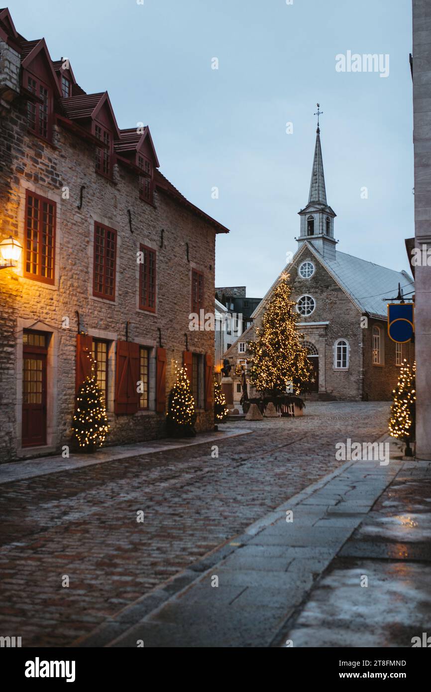 Eine idyllische Kopfsteinpflasterstraße in Quebec, Kanada, mit funkelnden Weihnachtslichtern und einem prachtvoll beleuchteten Baum in der Nähe historischer Gebäude in der Abenddämmerung. Stockfoto