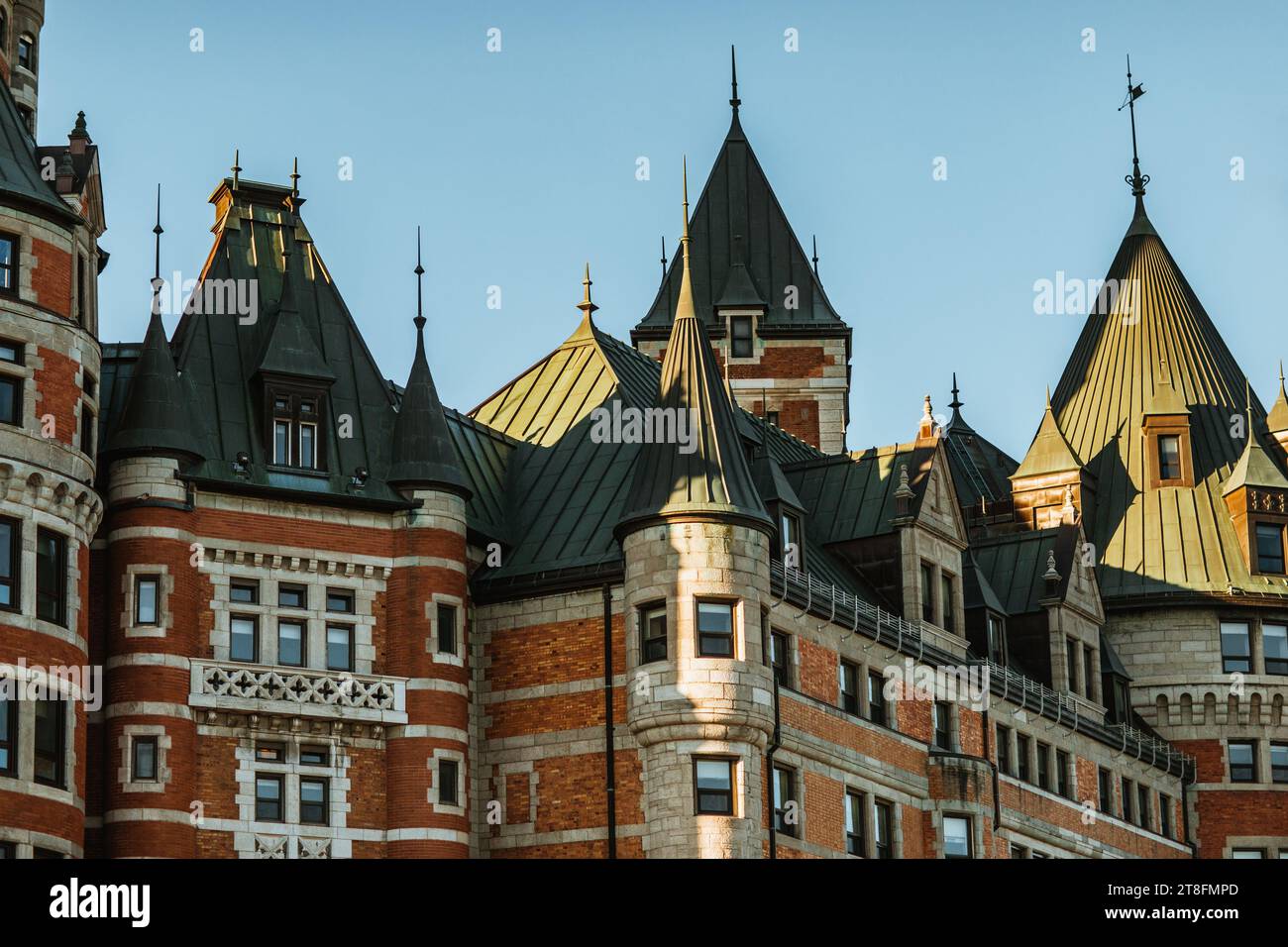 Das warme Leuchten der untergehenden Sonne beleuchtet die kunstvollen Details der Türme und Türme einer großen europäischen Burg in Quebec, Kanada Stockfoto