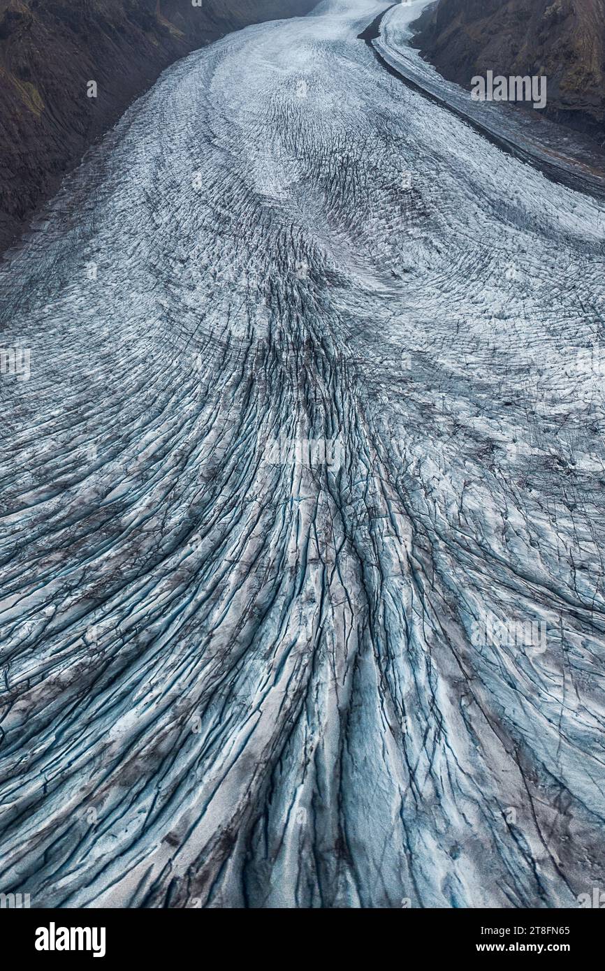 Von oben Schuss eines Gletschers, der durch ein Tal mit markanten blauen Eismustern fließt Stockfoto