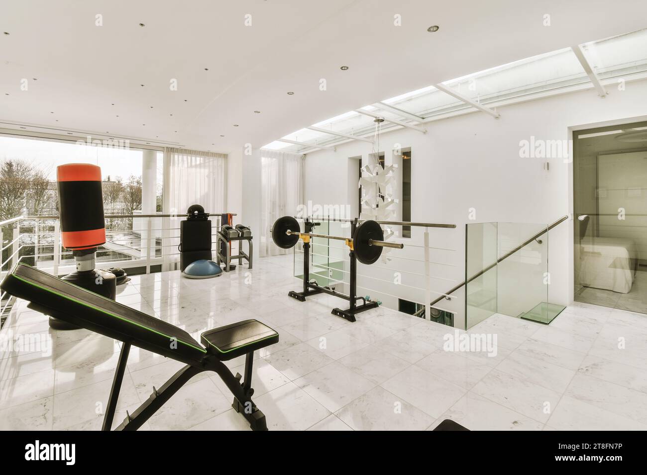 Das Innere des Fitnesscenters mit verschiedenen Fitnessgeräten vor dem Fenster in einem modernen Haus mit weißen Wänden Stockfoto