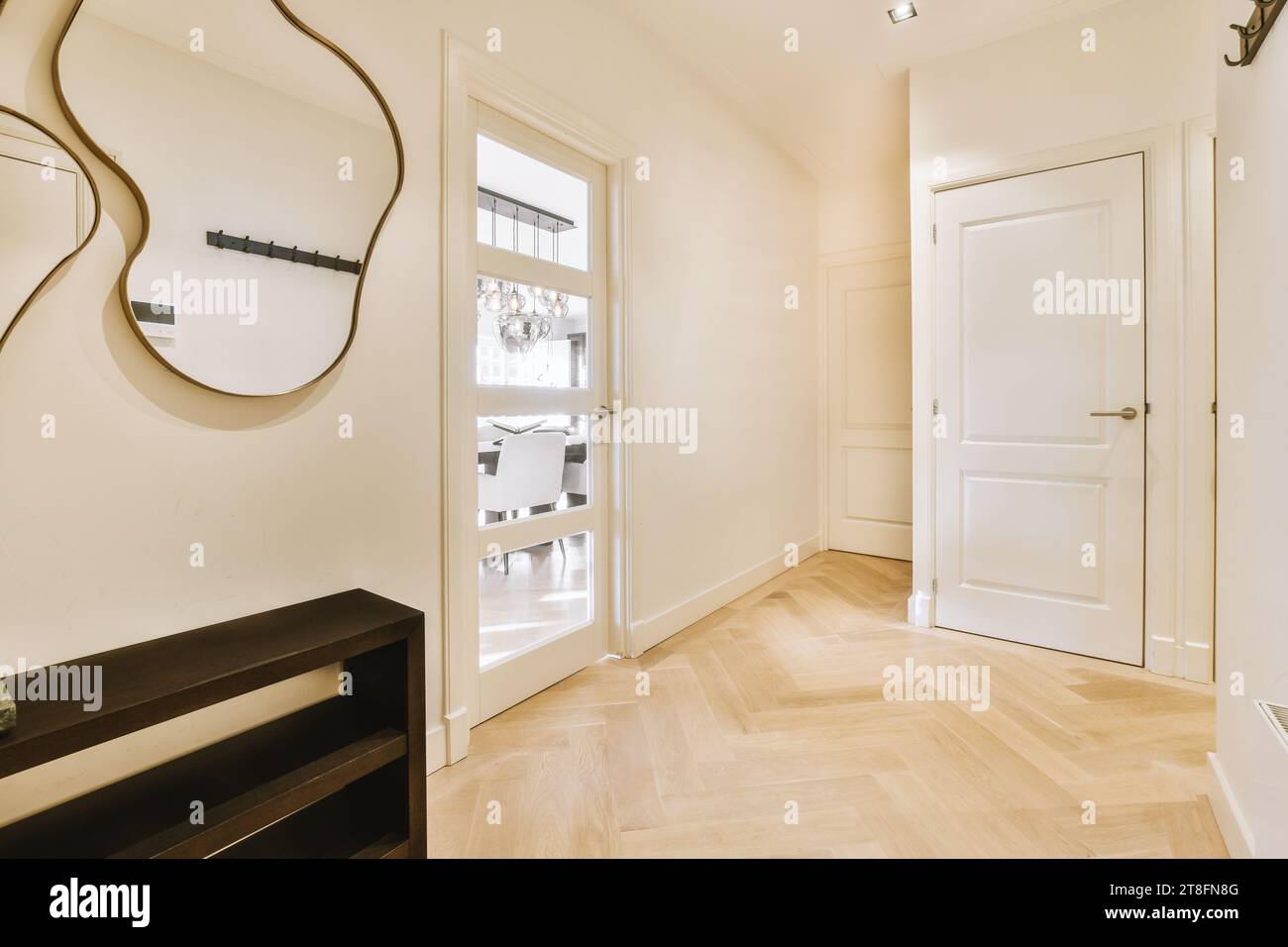 Leerer Flur mit Spiegel an der weißen Wand und geschlossenen Türen verschiedener Zimmer in einem modernen, zeitgenössischen Haus Stockfoto
