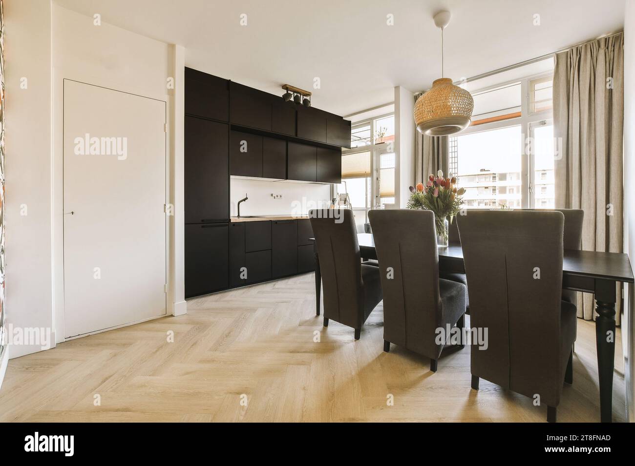 Esstisch und Stühle mit Blumenvase sind vor einer offenen, modernen Küche mit Fenster zu Hause angeordnet Stockfoto