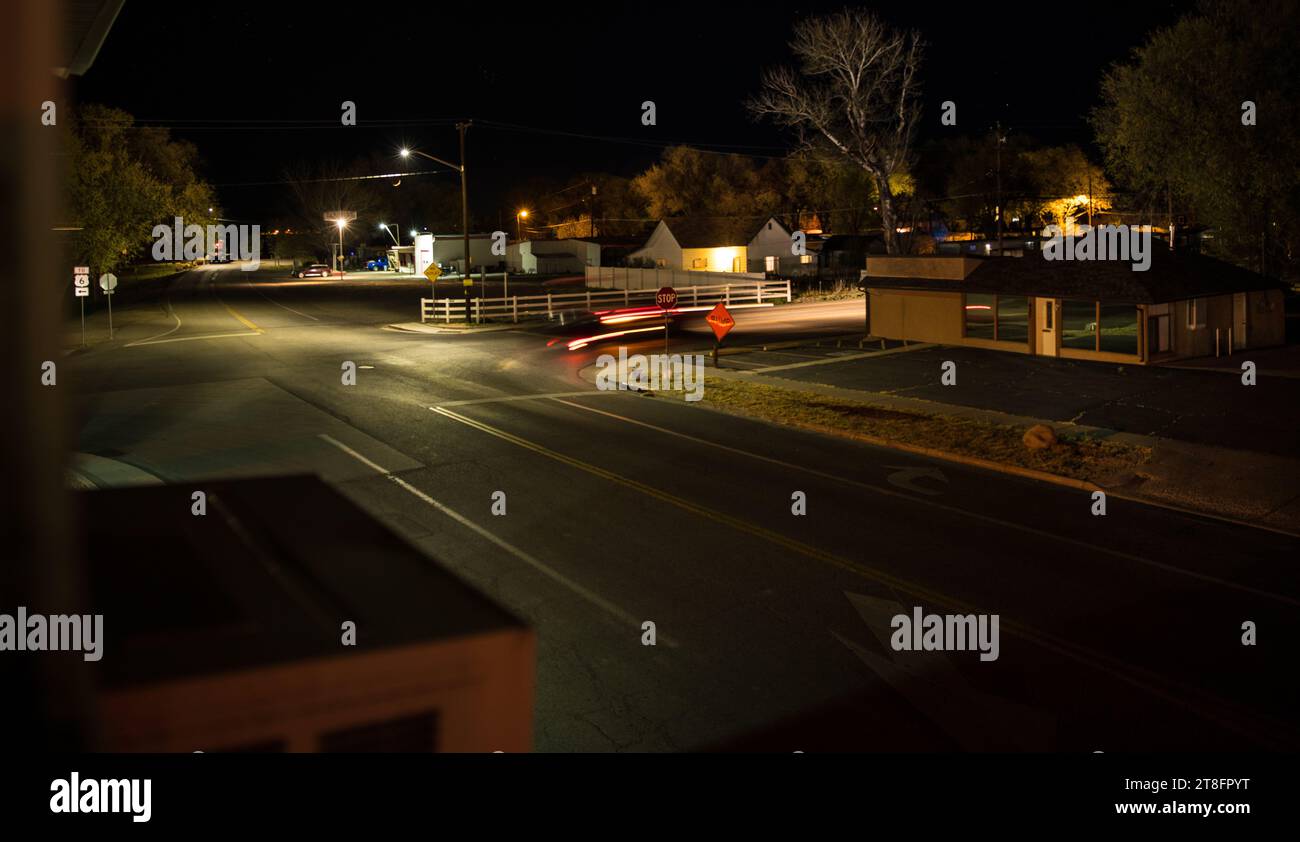 Mondsichel mit Ursa Major (großer Bär) aus einem Fenster im Obergeschoss mit Blick auf eine Kreuzung mit vier Haltestellen in der kleinen Stadtgegend in der Abenddämmerung. Stockfoto