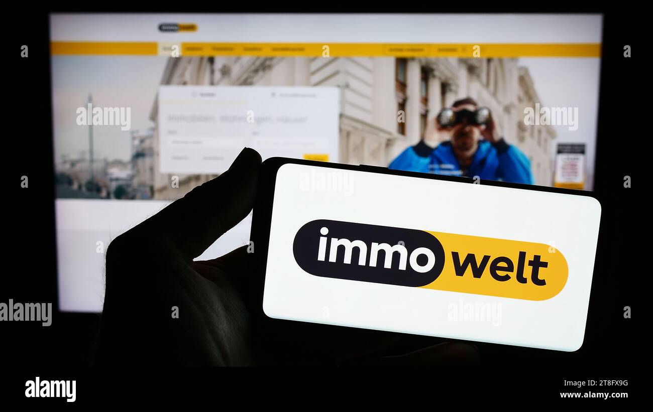 Person mit Smartphone mit Logo der deutschen Immobilienplattformgesellschaft immowelt GmbH vor der Website. Schwerpunkt auf dem Display des Telefons. Stockfoto