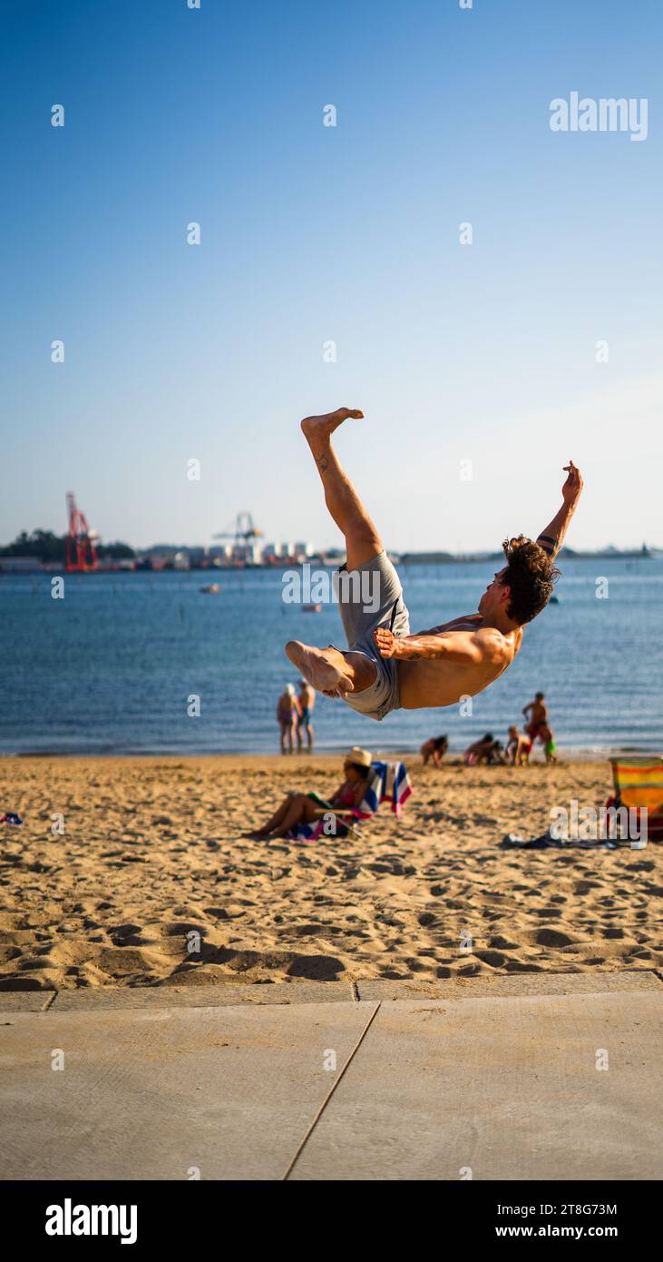 Teen Boy Parkour Somersaults Teen Boy Parkour springt von der Wand in Somersaults und flippt in den blauen Himmel am Strand Stockfoto