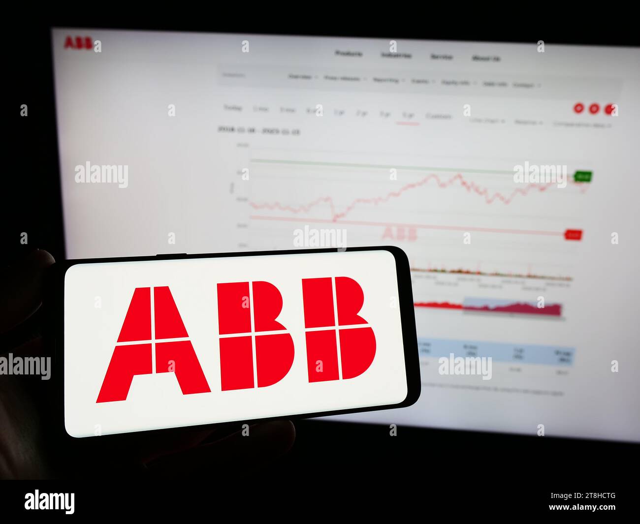 Person, die ein Mobiltelefon mit dem Logo des Elektrogeräteunternehmens ABB Ltd. Vor der Webseite des Unternehmens hält. Schwerpunkt auf dem Display des Telefons. Stockfoto