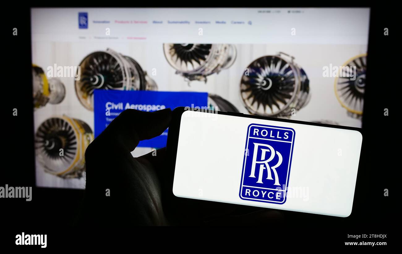Person, die ein Mobiltelefon mit dem Logo des britischen Luftfahrtunternehmens Rolls-Royce Holdings plc vor der Business-Website hält. Schwerpunkt auf dem Display des Telefons. Stockfoto
