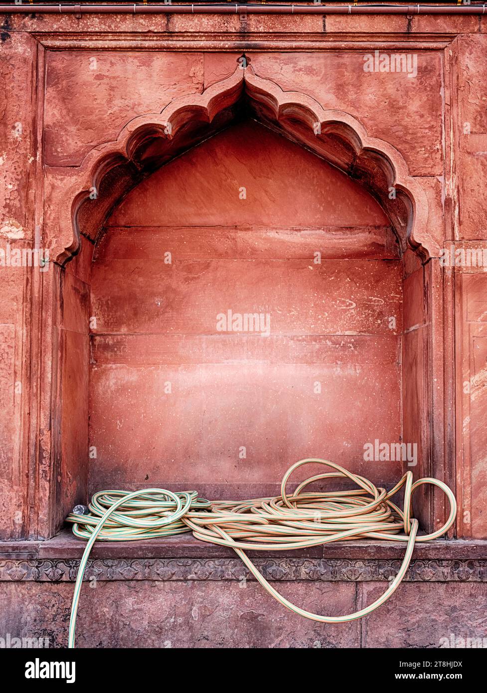 Gelbe Wasserschläuche sind lose in einer Wandnische der Jama Masjid Moschee in Delhi, Indien, gewickelt. Stockfoto