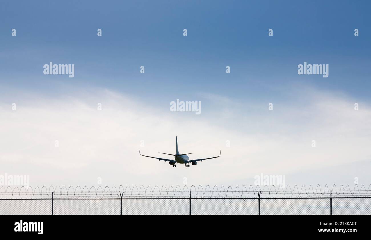 Rückansicht eines kommerziellen Flugzeugs, das über Stacheldrahtzaun fliegt Stockfoto
