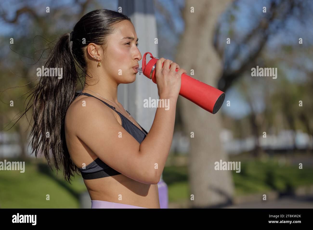 Porträt eines lateinischen Mädchens in Sportbekleidung Trinkwasser aus einer roten Flasche. Stockfoto