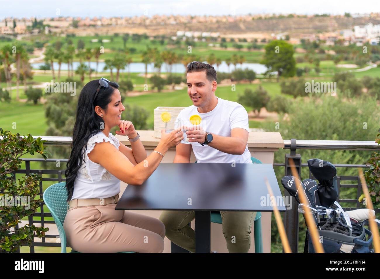 Zwangloses reiches Paar, das mit Cocktails auf einer Außenterrasse mit Blick auf einen Golfplatz lockt Stockfoto