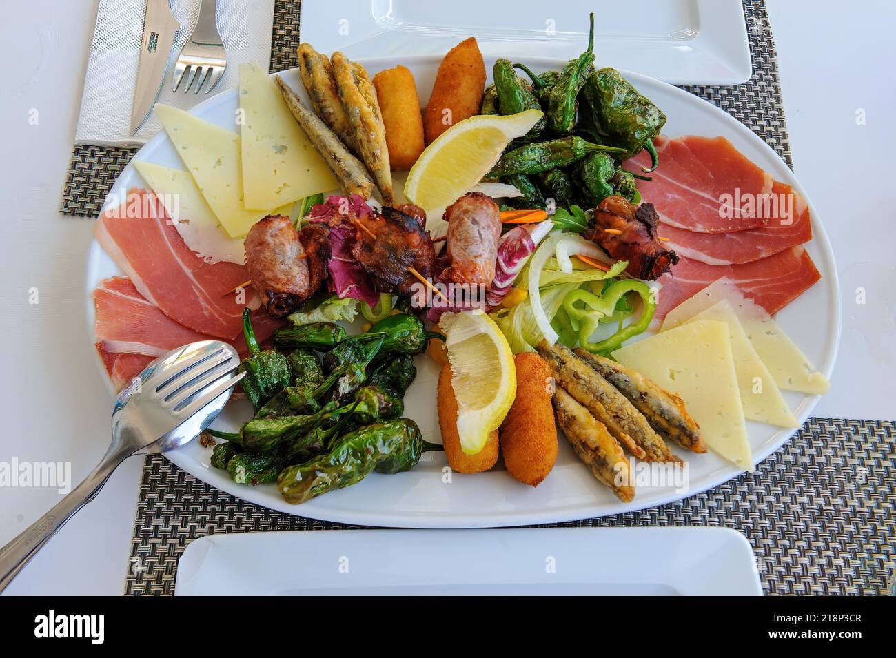 Vorspeiseteller auf gedecktem Tisch mediterranes italienisches Gericht Appetiser auf großem Teller roher Schinken, Käsescheiben, Paprika, Fisch auf Stäbchen gebraten Stockfoto