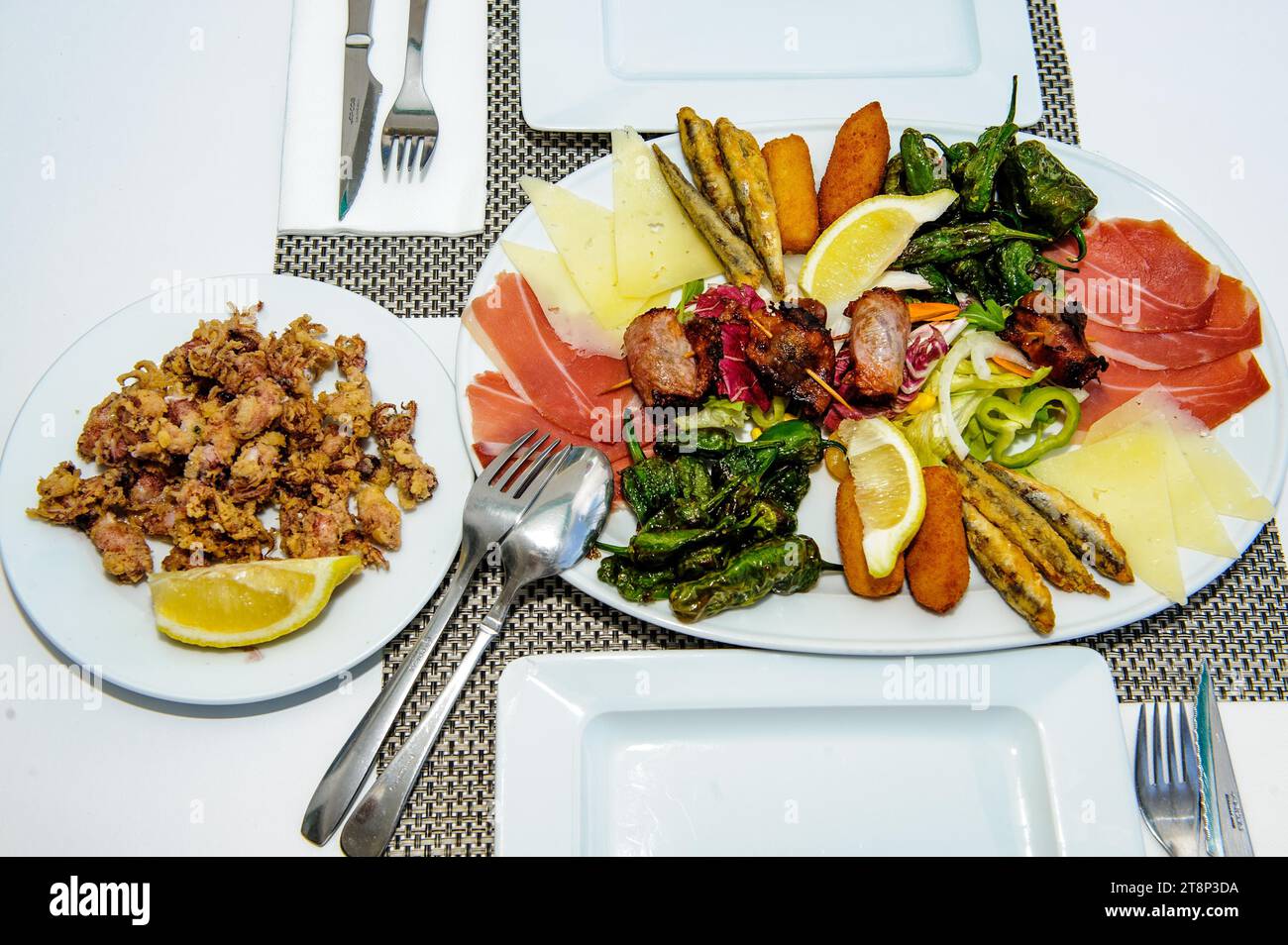 Vorspeiseteller auf gedecktem Tisch mediterranes italienisches Gericht Appetiser mit kleinen, frittierten Kalamari links, auf einem großen Teller roher Schinken, Käse Stockfoto