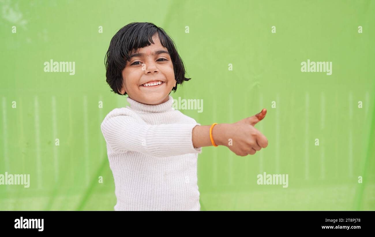 Glückliches positives kleines Mädchen in weißem Rollkragen, das Daumen nach oben wie Geste zeigt, isoliert auf einfachem Pastellhintergrund hellgrünem Studioporträt. Stockfoto