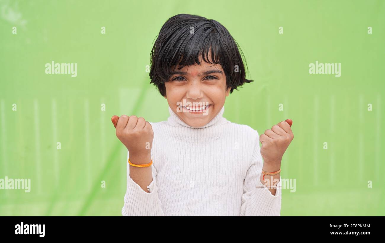 Süßes asiatisches Mädchen, 6 bis 7 Jahre alt, schwarzes Haar, weißes ärmelloses Hemd. Sie ballte ihre Fäuste und hob beide Arme, um die Muskeln im A zu zeigen Stockfoto