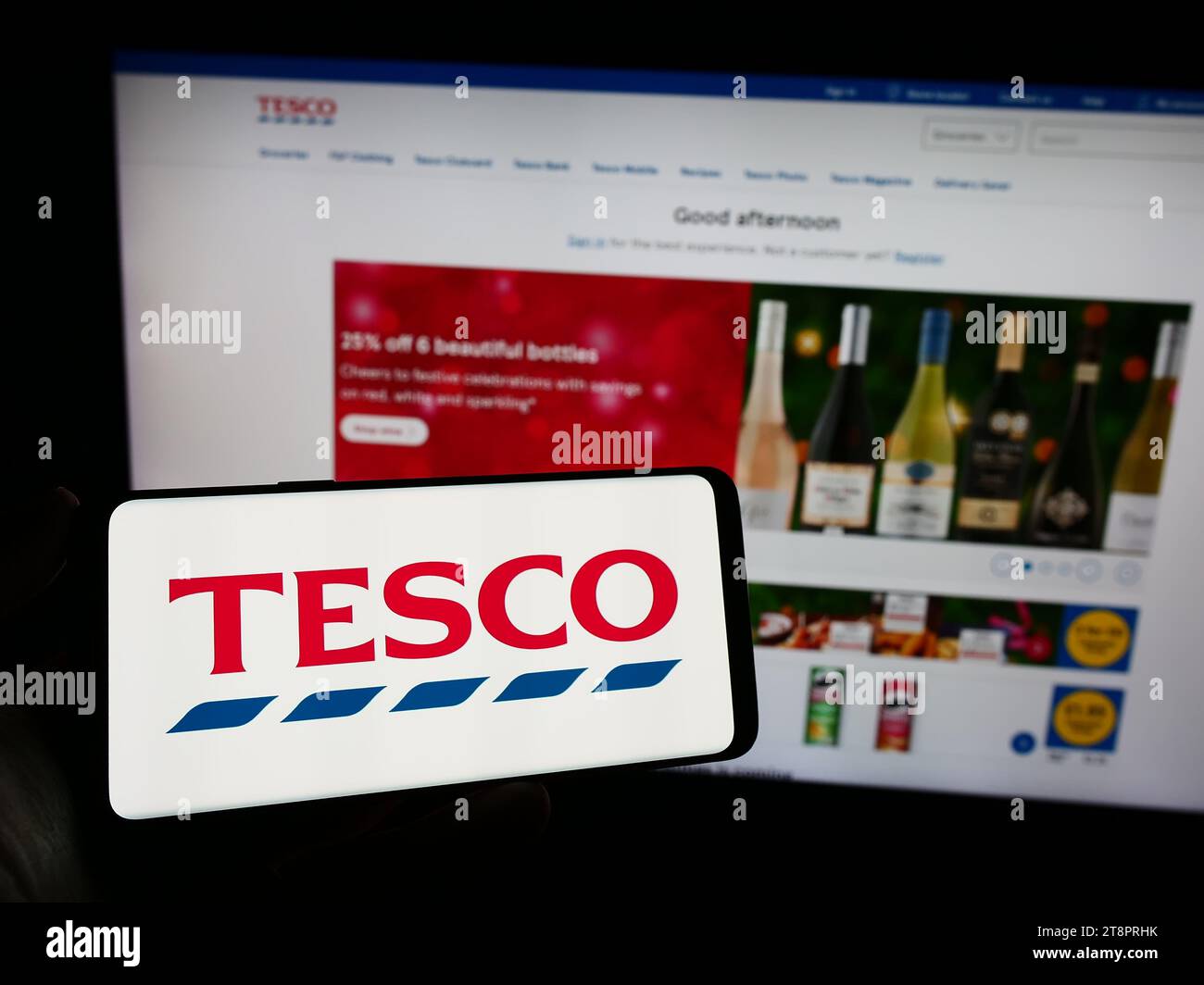 Person, die ein Mobiltelefon mit dem Logo des britischen Lebensmitteleinzelhandelsunternehmens Tesco plc vor der Webseite hält. Schwerpunkt auf dem Display des Telefons. Stockfoto