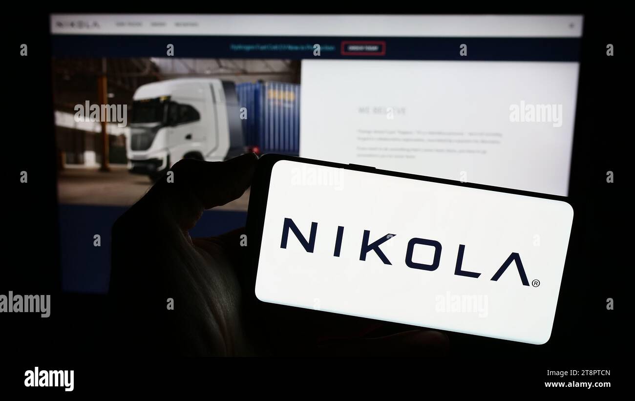 Person, die ein Mobiltelefon mit dem Logo des amerikanischen Elektrofahrzeugunternehmens Nikola Corporation vor der Webseite hält. Schwerpunkt auf dem Display des Telefons. Stockfoto