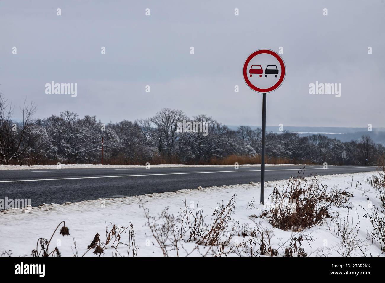 Verschneite Straße mit Verkehrsschild Überholverbot. Straße auf dem Land. Stockfoto