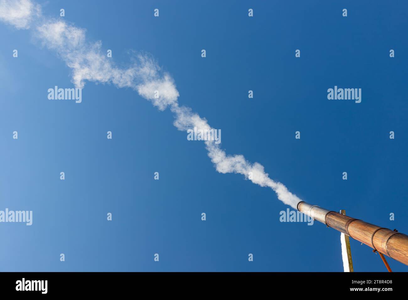 Eine Rauchfahne oder Dampf aus einem industriellen Schornstein an einem klaren blauen Himmel. Stockfoto