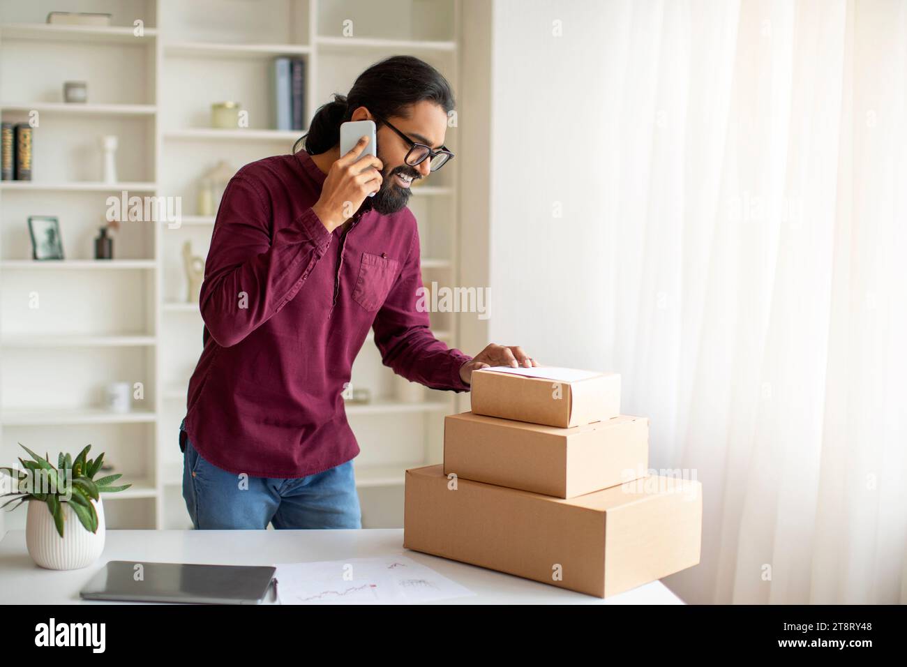 Kleine Unternehmen. Indischer Mann, Der Bestellungen Packt Und Zu Hause Telefoniert Stockfoto