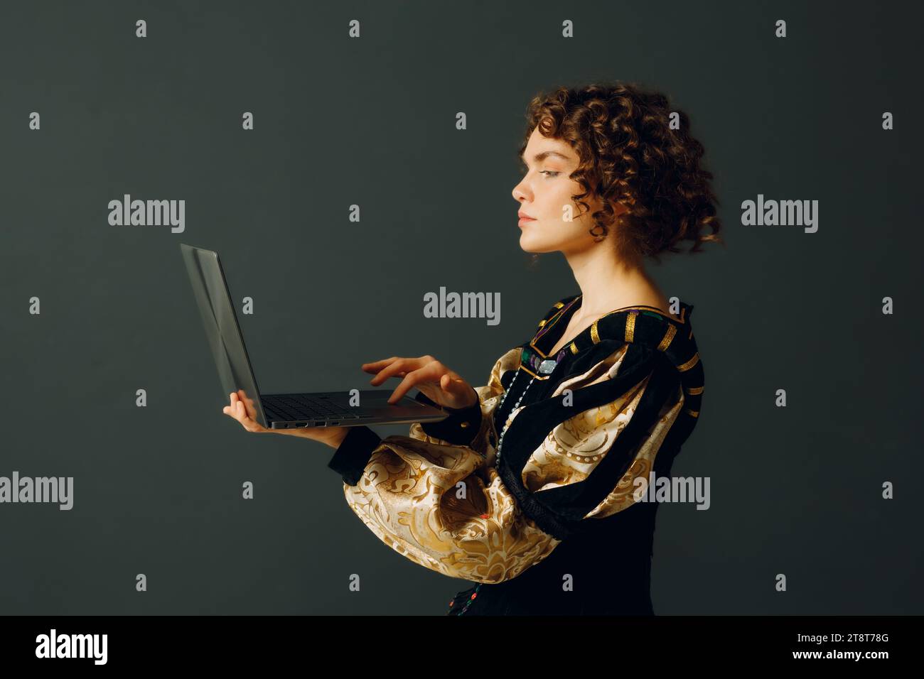Junge Erwachsene Frau in einem mittelalterlichen Kleid, die an einem Laptop arbeitet. Profil Hochformat Stockfoto