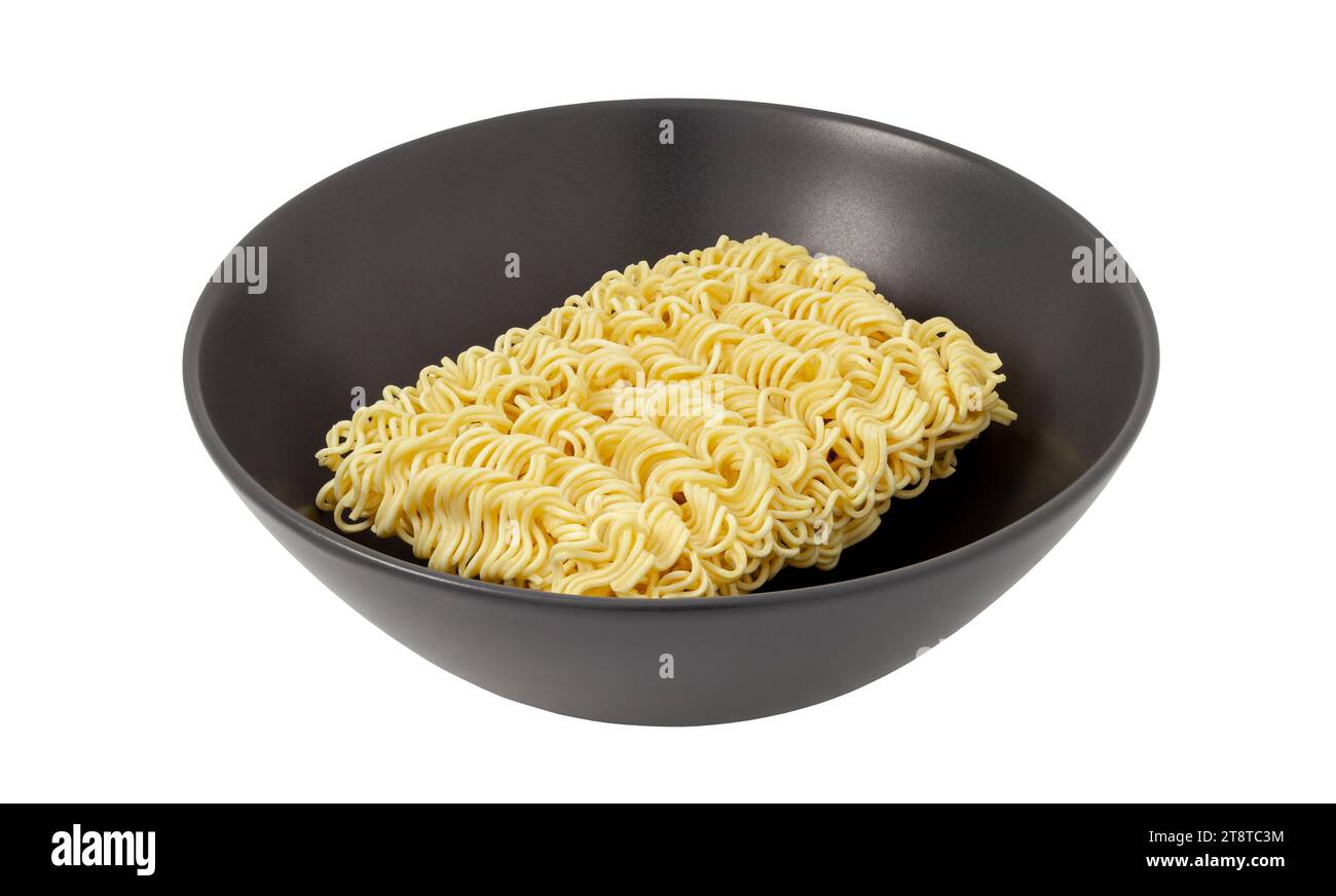Nudeln Instant roh, ungekochtes Stück, Brikett in dunkler Schüssel isoliert auf weißem Hintergrund mit Schneidepfad. Stockfoto